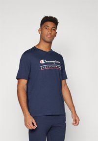 Navy blue cotton t-shirt featuring a white "Champion" logo with red accents. Short sleeves and a classic crew neck design.