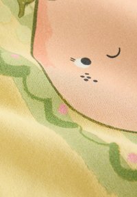 Produsul prezintă o prim-plan cu o țesătură moale într-o paletă de culori pastelate. Designul include un chip zâmbitor cu accente roz și modele verzi în formă de spirale.