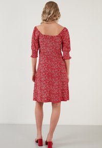 Robe rouge à fleurs avec manches courtes bouffantes, un décolleté carré et un ourlet évasé. Le tissu présente de petits motifs floraux blancs et roses.