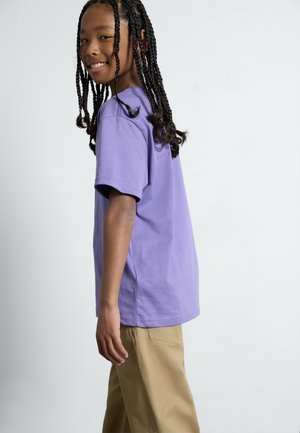 Camiseta de algodón morada de manga corta y corte relajado. Combinada con pantalones beiges. Sin patrones visibles ni herrajes distintivos.