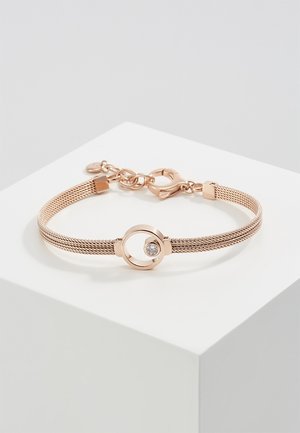 Bracelet en maille or rose avec un charm circulaire orné d'une pierre précieuse claire flottante, présenté sur un socle géométrique blanc.