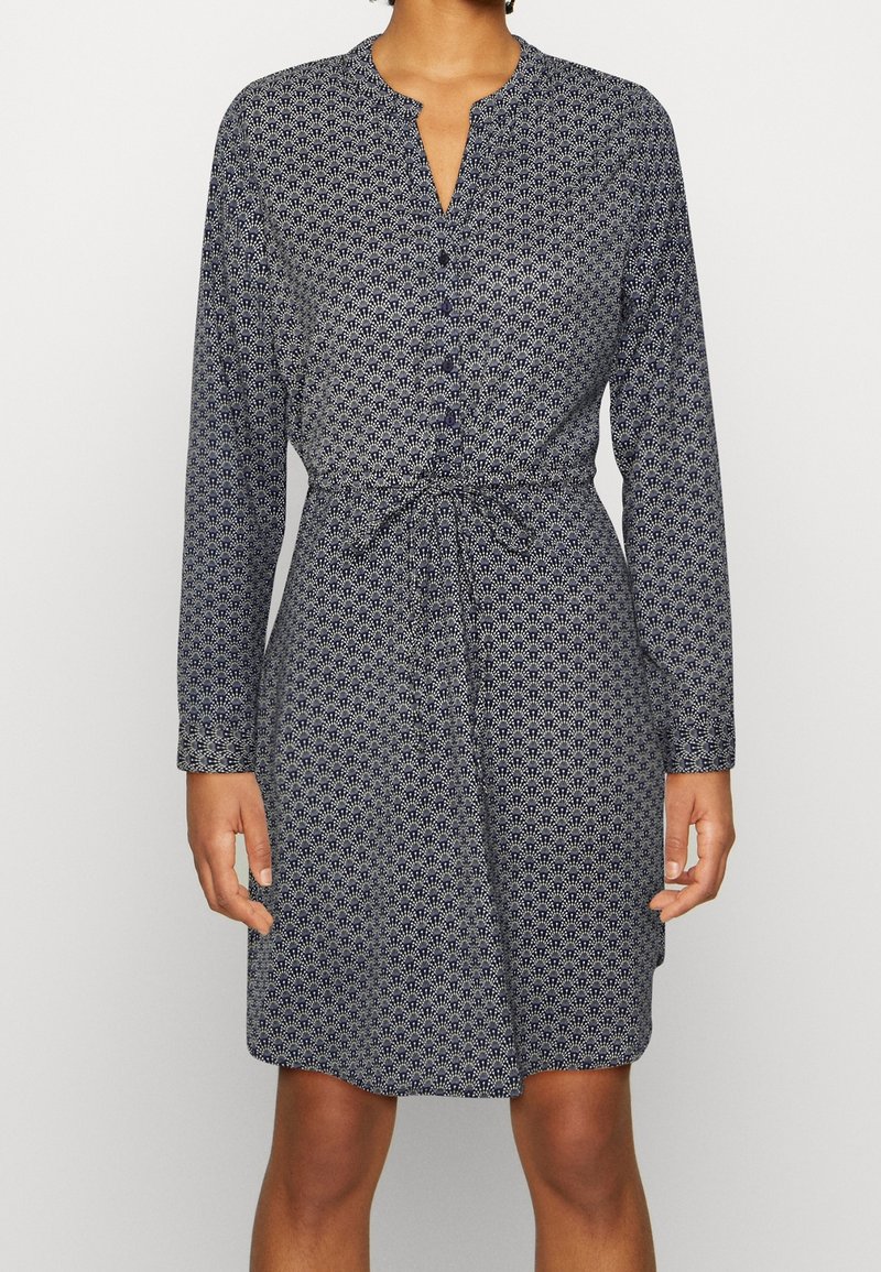 Robe boutonnée bleu marine avec un motif floral blanc, manches longues, encolure ronde et détail à la taille nouée. Texture de tissu lisse.