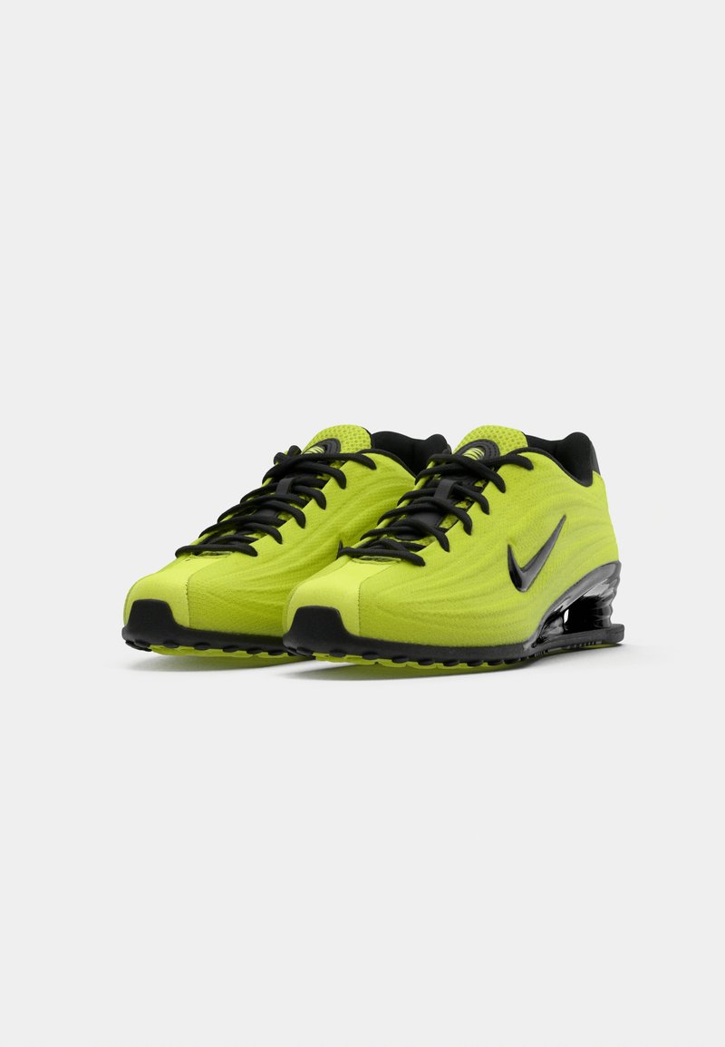 Ett par klara gula och svarta Nike-löparskor med synlig luftkudde i sulan och svarta skosnören, visade i vinkel mot en vit bakgrund.