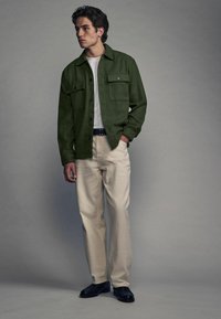 Grøn flannel skjorte med to frontlommer, parret med beige bukser og sorte sko. Ensfarvet hvid t-shirt under. Afslappet pasform.