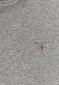 Szara bawełniana koszulka z okrągłym dekoltem, delikatną teksturą oraz wyszywanym logo "GANT" z herbem na piersi.