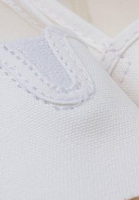 Tissu blanc avec une surface texturée et des coutures visibles. Comprend une sangle Velcro pour le maintien, soulignant un design simple et fonctionnel.