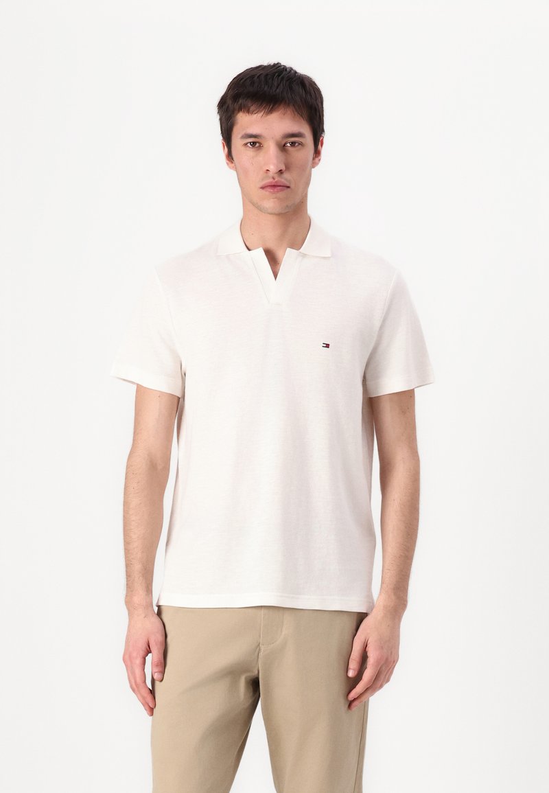 Pánské polo tričko s krátkým rukávem z krémové bavlny, s výstřihem do V a malým logem na hrudi. Úzký střih, hladká textura a decentní design.