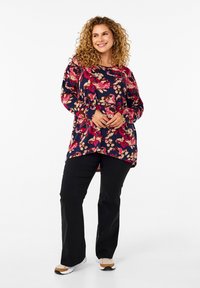 Tunic navy a maniche lunghe con un motivo floreale multicolore, orlo curvo e vestibilità comoda, abbinata a pantaloni neri e sneakers bianche.