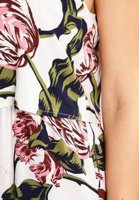 Blommig klänning med vit bakgrund och rosa och gröna tulpanmönster. Lättviktig tyg, lagerdesign överst och mjuk textur.