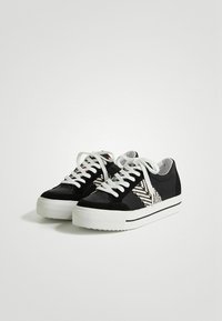 Sneaker in suede nere con suola in gomma bianca, lacci bianchi e un accento in tessuto decorato sui lati. Design a taglio basso.