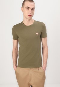 Olivenfarvet kortærmet t-shirt med rund halsudskæring og lille rødt trekantlogo på brystet, lavet af et glat bomuldsstof.