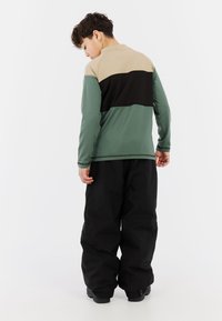 Langsleeve shirt met een groen, beige en zwart kleurblokdesign. Gecombineerd met losse zwarte broek en laarzen, wat praktische stijl laat zien.