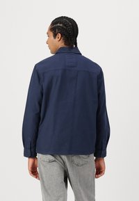 Navy blue cotton shirt with a back collar, buttoned cuffs, and a relaxed fit. Textured, lightweight with a simple design.
