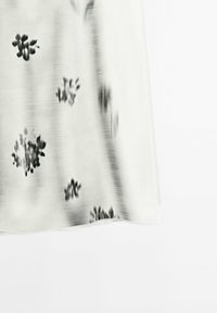 Tissu blanc avec des imprimés floraux abstraits noirs et des rayures verticales brossées, présenté sur un fond blanc uni.
