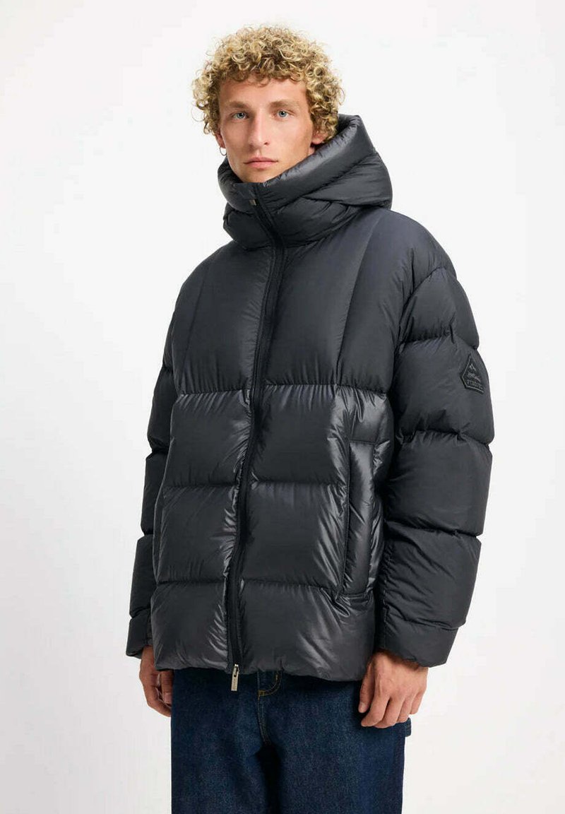 Giacca imbottita nera con collo alto, design trapuntato e chiusura con cerniera. Notevole per il materiale lucido e per la toppa con logo sulla manica.