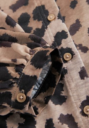 Dierprint shirt in beige en zwart stof, met knopen en een geraffineerd detail bij de manchet, dat een gestructureerd oppervlak ontwerp laat zien.