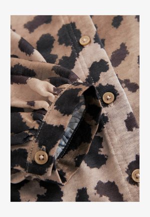Camisa de estampado animal en tela beige y negra, con botones y detalle fruncido en el puño, mostrando un diseño de superficie texturizada.