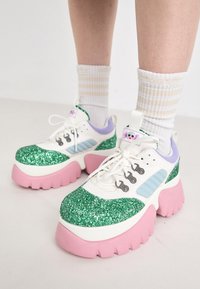 Plattform sneakers med hvit og pastellfargeskjema, grønn glitter overdel, rosa såle og flere hull. Har lekne detaljer.