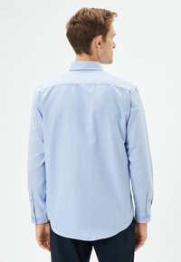Lyseblå langærmet skjorte lavet af et glat, let stof, med rygpanel og knapmansjetter. Rundet kantdetalje.