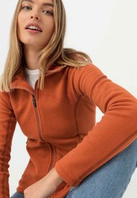 Orange Fleecejacke mit hohem Kragen und Reißverschluss, mit gesteppten Details und weicher Textur, kombiniert mit lässiger Jeans.