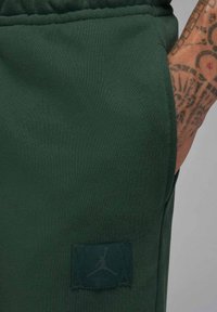 Pantaloncini sportivi verdi con tessuto strutturato, caratterizzati da una vistosa toppa con il logo Jordan verde scuro sul lato e una cintura elastica.