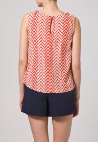 Top senza maniche rosso e crema con un motivo a zigzag, scollo rotondo, schiena con apertura a chiave e un taglio comodo. Abbinato a pantaloni corti blu navy.