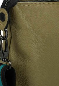 Groene gestructureerde leren tas hoek met zwarte rits en metalen hardware. Inclusief een blauw en bruin gestreepte schouderband aan de zijkant bevestigd.