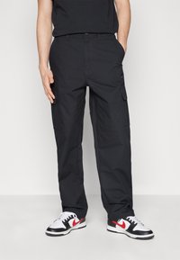 Svarta cargobyxor med en strukturerad tygkvalitet, med sidofickor och en avslappnad passform. Matchas med svartvita sneakers med röda detaljer.