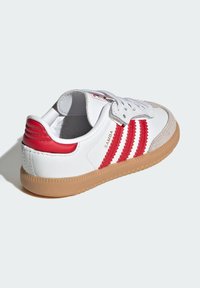White sneakers with red stripes and accents, suede toe cap, and a gum rubber outsole. Laces and padded collar for comfort.