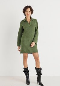 Grønt strikket kjole med v-utringning, lange ermer og ribbestrikket hem. Brukt med svarte knelange, slouchy hælboots.