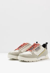 Beige sneakers med mesh- och lädermaterial. Har flerfärgade snören, svarta accenter och texturerade sulor.