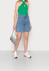Grön halterneck-top med ett nyckelhål, blå denim Bermudashorts, zebra-randig handväska och vita sneakers med rosa detaljer.