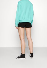 Felpa verde menta con vestibilità rilassata, pantaloni corti neri e sneakers alte nere. Presenta polsini e orlo a coste, cuciture a vista sui pantaloni corti.