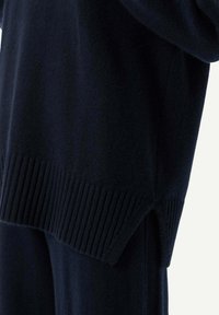 Mörkblå stickad tröja med ribbat avslut och sidofickor, tillverkad av mjukt, strukturerat tyg för ökad komfort.