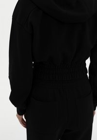 Mustat hupparit ja yhteensopivat verkkarit, joissa on rento malli, elastinen vyötärö ja sivutaskut, esittelevät sileää kankaan pintaa.