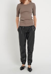 Brązowa, prążkowana bluzka z krótkim rękawem połączona z czarnymi skórzanymi joggerami z elastycznymi mankietami i kieszeniami, uzupełniona czarnymi, spiczastymi balerinami.