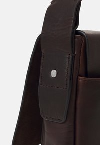 Borsa in pelle marrone con texture liscia, bordi cuciti e chiusura a scatto con dettaglio in metallo del logo. Design strutturato con tasca laterale.