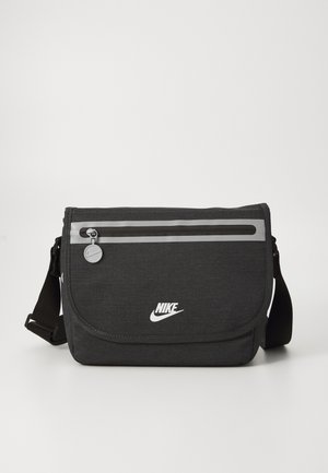 Black messenger bag with a smooth texture, adjustable strap, front zip pocket, reflective strip, and Nike logo in white.