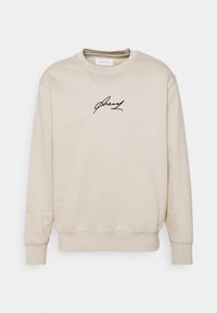 Beige sweatshirt lavet af blødt stof, med rund halsudskæring, ribbede manchetter og et sort signaturtryk på forsiden.