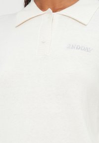 Sweter polo w kolorze off-white z prążkowanym kołnierzykiem, z dwoma guzikami i subtelnym logo "2ND DAY" w szarym kolorze po lewej stronie na piersi.