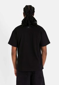 Zwarte katoenen T-shirt met een ontspannen pasvorm, korte mouwen en een vierkante halslijn, met een klein label aan de achterkant en een zachte textuur.