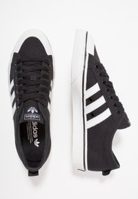 Svarta kanvas sneakers med vita ränder, rund tå, snörningsdesign, kontrasterande vit gummisula och texturerad tyg.