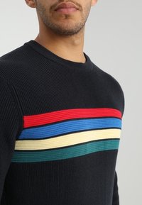 Pull en tricot noir avec des rayures horizontales rouges, bleues, jaunes et vertes. Texture côtelée et col rond classique.