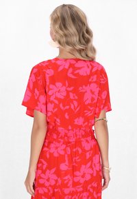 Abito rosso a fiori con motivo di grandi fiori rosa, maniche corte, vita arricciata, gonna fluida e tessuto leggero e morbido.