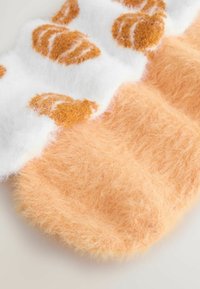 Weiche, flauschige Socken, eine in einfarbig Pfirsich und die andere weiß mit braunen Flecken, flach auf einer hellen Oberfläche liegend.