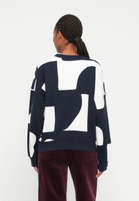 Sudadera de rayas en azul marino y blanco con un corte holgado, cuello redondo y puños acanalados, combinada con pantalones de pana burdeos.