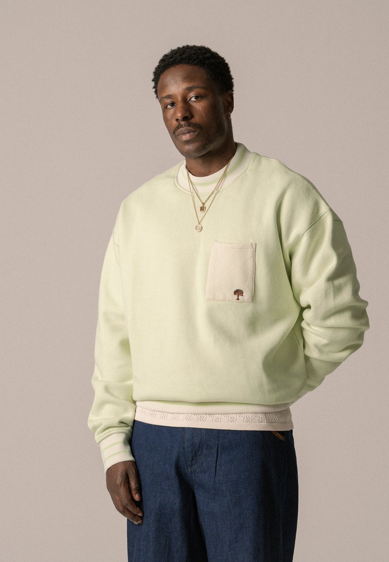 Jasnozielony sweatshirt z kieszenią z przodu i haftowanym logo drzewa, w zestawie z ciemnoniebieskimi spodniami z fakturowanym pasem.