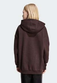 Felpa marrone oversize con cappuccio ampio, tessuto strutturato e spalle scese, con bordi a coste su orlo e polsini.
