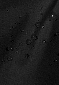 Waterdruppels verspreid over glad, zwart waterafstotend stof met zichtbare textuur en lichte plooien.