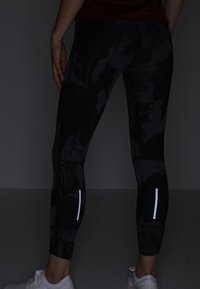 Black athletic leggings with a glossy texture, featuring reflective accent stripes on the lower legs, designed for performance and comfort.